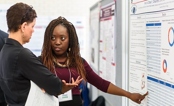 A UIC School of Public Health student explains a research poster to a staff member at a research event.